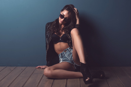 Stunning young woman with dark hair posing at the floor  with a perfect body looking down through sunglassesの写真素材