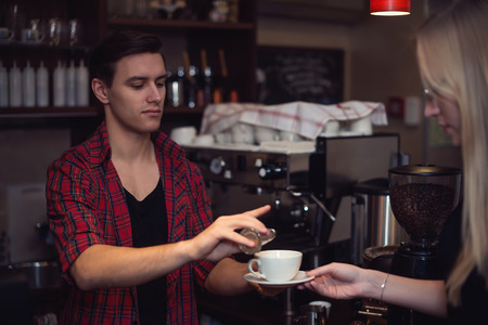 Hipster barista in  plaid shirt adds cinnamon in customers cofeeの写真素材