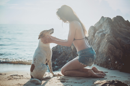 Portrait of beautiful happy young woman sitting playing with her pet dog sunset at the beach on the sea shore twilight sky as background.の写真素材