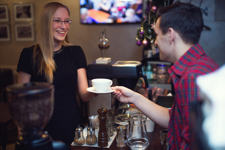 Pretty blond girl taking her order with pleasant smile. Barista is passing her cup pf cofee.の写真素材