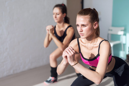 two girls doing squats together indoors training warm up at gym fitness, sport and lifestyle concept.の写真素材