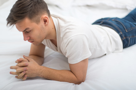 good looking man in white T-shirt and blue jeans lying on his bed at home.の写真素材