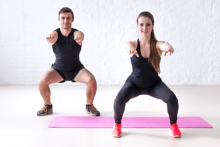 Fitness man and woman exercising squat exercise hands behind head looking at camera concept sport, training, warming up and lifestyle.の写真素材