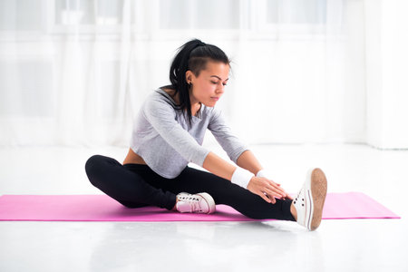 Fit woman doing aerobics gymnastics stretching exercises her leg and back to warm up at home on yoga...