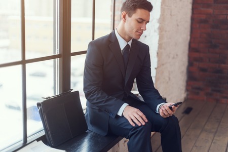 Businessman sitting waiting looking at mobile phone.の写真素材