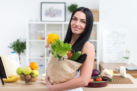 Close-up portrait of a woman holding paper bag full of fresh vegetables. Happy smiling female vegetarian with fresh groceryの写真素材