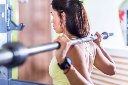 Fit woman doing squat with barbell in the gym