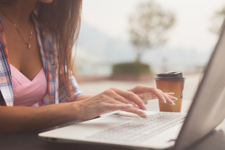 Close up shot of female hands typing on a laptop keyboard. Young woman studying and working in the park.の写真素材