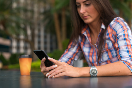 Young woman sitting outdoors reading and typing messages on her smartphoneの写真素材