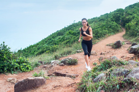Sporty young woman in black sportswear trail running on mountain nature path. Fit girl jogging downhill on rocky trackの写真素材