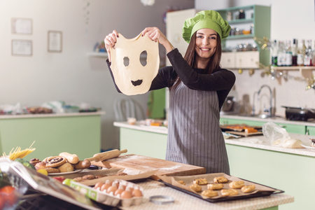 Young housewife having fun holding funny dough face while baking pastry in the kitchenの写真素材