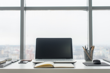 Workplace with notebook laptop Comfortable work table in office windows and city view.の写真素材