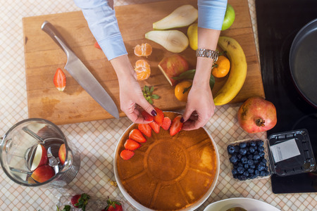 Top view of woman decorating a cake layer with strawberry. Housewife cooking fruit pieの写真素材