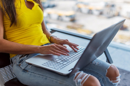 Cropped image of young woman holding a laptop on lap typing  keyboard indoors in  public placeの写真素材