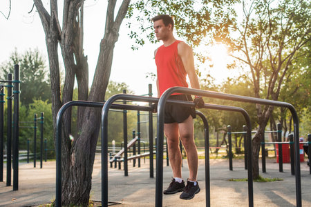 Fit man doing triceps dips on parallel bars at park exercising outdoors