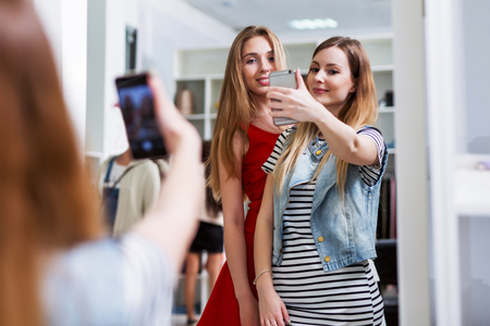 Two smiling girls taking selfie while shopping in a clothing storeの写真素材