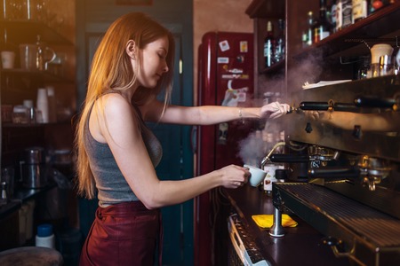 Stylish ginger girl making coffee using a professional coffee machine in coffee houseの写真素材