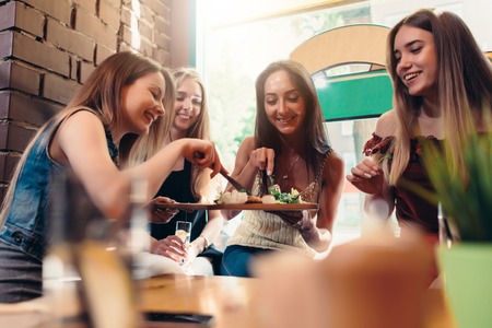 Group of laughing pretty young women sharing food sitting at coffee shopの写真素材