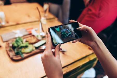Food photography for social networks. Close-up image of female hands holding phone with food on screen taking picture of healthy mealの写真素材