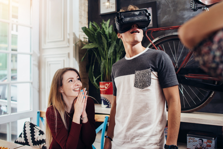 Emotional teenagers using VR headset to watch 3D films or play games hanging out at homeの写真素材