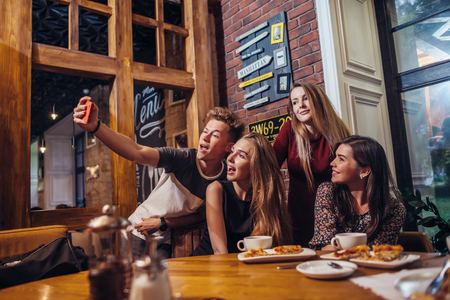 Excited friends taking selfie with smartphone sitting at table having night out.の写真素材