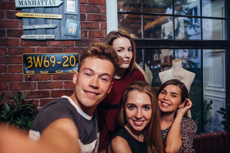Friends taking self-portrait photograph, guy holding a camera shooting selfie with his female friends hanging out.の写真素材