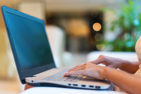 Female hands typing on keyboard. Cropped photo of a young woman holding laptop her knees and working.の写真素材