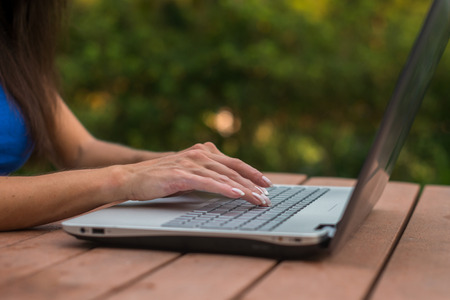 Close-up view of female hands on laptop keyboard. Student learning outdoors.の写真素材
