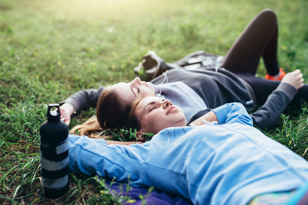 Two young sportswomen laying on grass with eyes closed relaxing after outdoor workoutの写真素材