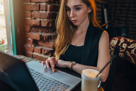 Portrait of young female freelancer drinking coffee working on laptop sitting in fashionable restaurantの写真素材