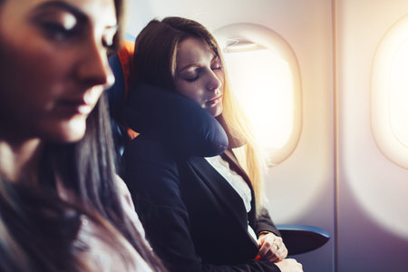 Two businesswomen sleeping in the airplane using neck cushion while going on business trip