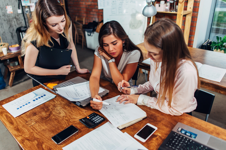 Three female economists checking documentation analyzing documents sitting at desk in modern officeの写真素材