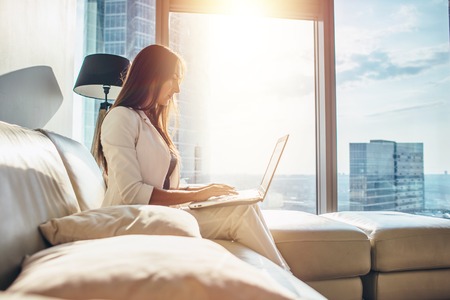 Side view of successful young female entrepreneur wearing formal business attire working on netbook at her luxurious apartmentの写真素材