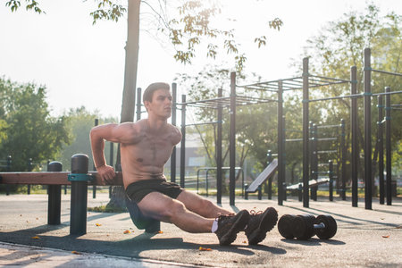 Young fit man doing triceps dips exercises during outdoor cross training workout. Fitness male...