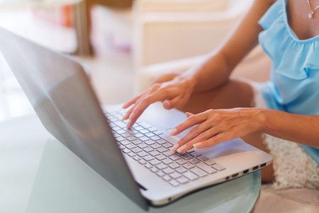Tanned young brunette European woman working on laptop, typing, surfing the web in white interior of...