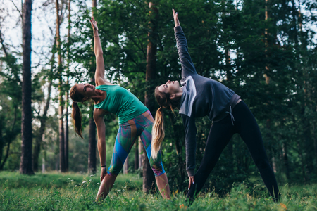 Female friends practicing yoga outdoors doing standing side bend or triangle pose in parkの写真素材