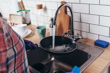Young woman wearing rubber gloves washing frying pan in kitchenの写真素材