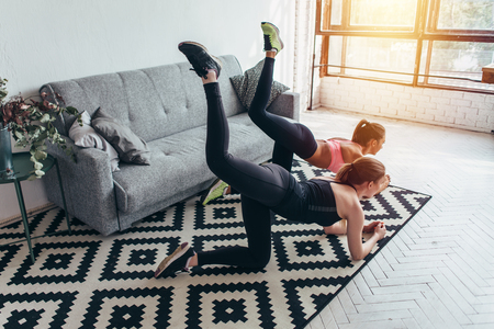 Two sportive female friends doing butt toning exercise performing donkey kicks at homeの写真素材