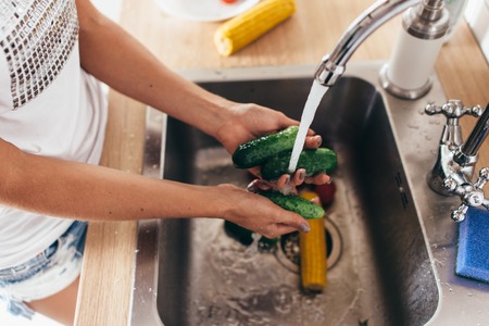 Woman washing cucumbers in kitchen sink close up.の写真素材