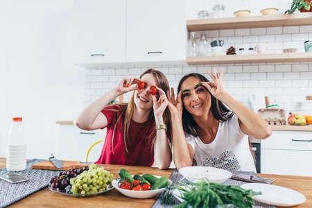 Girls fooling around in the kitchen playing with vegetables.の写真素材