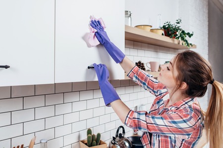 Woman in rubber gloves cleaning kitchen cabinetの写真素材