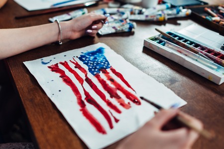 Young female illustrator drawing flag of the USA in using aquarelle paint sitting at workplaceの写真素材