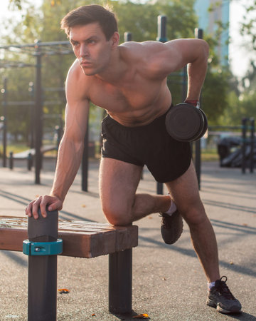 Muscular male athlete with arms raised doing lifting exercises dumbbells.