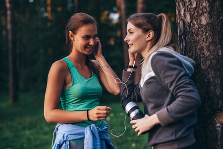 Two female runners relaxing after workout standing near the tree talking in parkの写真素材