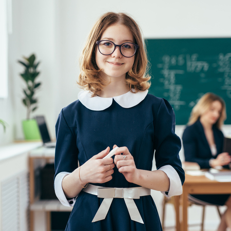 Portrait of smiling school girl with chalk in her hands standing in classroomの写真素材