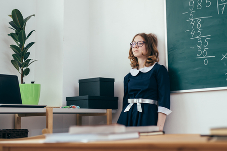 Sad schoolgirl standing in front of blackboard.