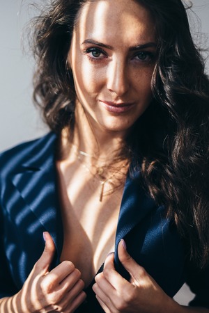 Photo of elegant woman in unbuttoned jacket with shadows on her bodyの写真素材