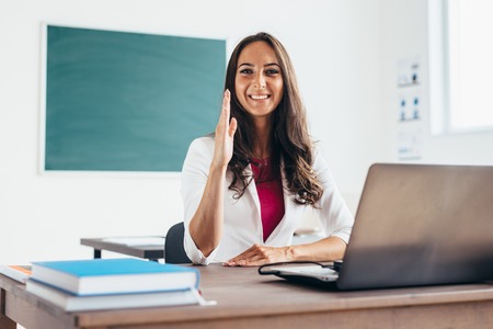 Girl raises hand sitting at the desk like a student.の写真素材