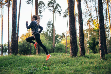 Young female athlete jogging in forest. Jogger doing morning physical training.