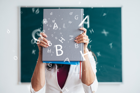 Female student standing near blackboard with bookの写真素材
